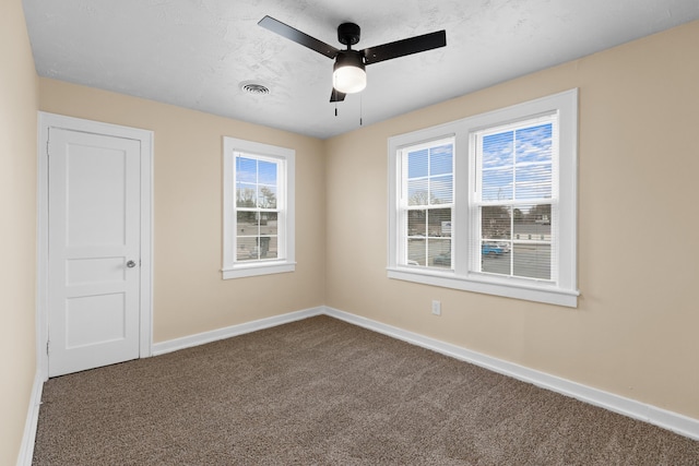 empty room with visible vents, baseboards, a ceiling fan, and dark carpet