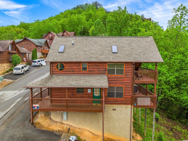 exterior space featuring roof with shingles, a view of trees, and log exterior