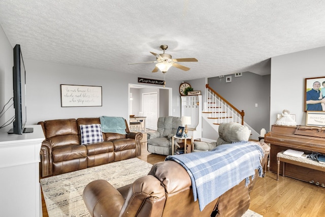 living area featuring stairway, light wood-style floors, a textured ceiling, and ceiling fan
