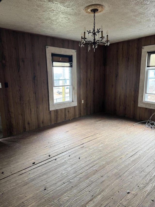 spare room with wooden walls, a chandelier, and a healthy amount of sunlight