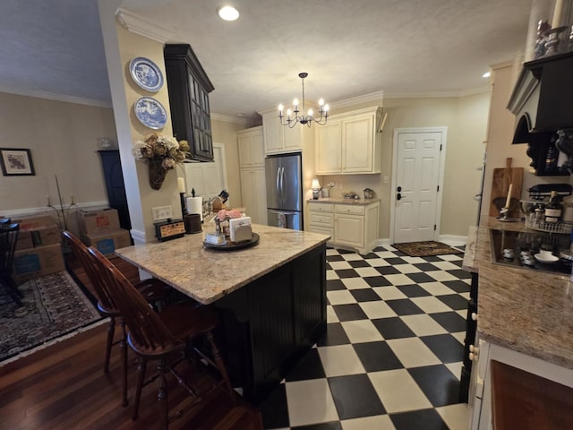 kitchen with an inviting chandelier, stainless steel fridge, a breakfast bar area, tile patterned floors, and ornamental molding