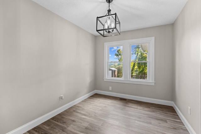 unfurnished dining area with light hardwood / wood-style floors, a textured ceiling, and an inviting chandelier