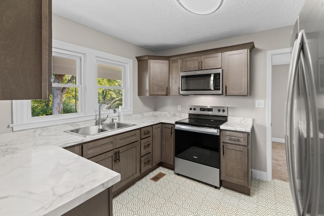 kitchen with a textured ceiling, light stone counters, sink, and stainless steel appliances