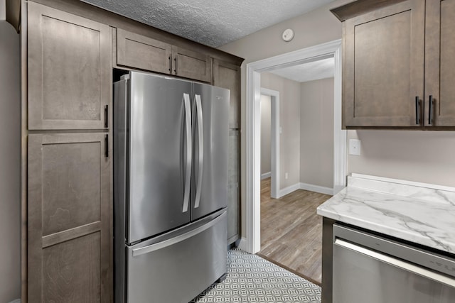 kitchen with light stone counters, dark brown cabinets, stainless steel appliances, and a textured ceiling