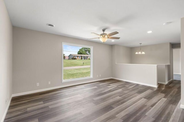 spare room with ceiling fan with notable chandelier and dark wood-type flooring