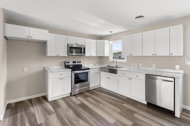 kitchen featuring white cabinetry, sink, hanging light fixtures, stainless steel appliances, and light stone counters