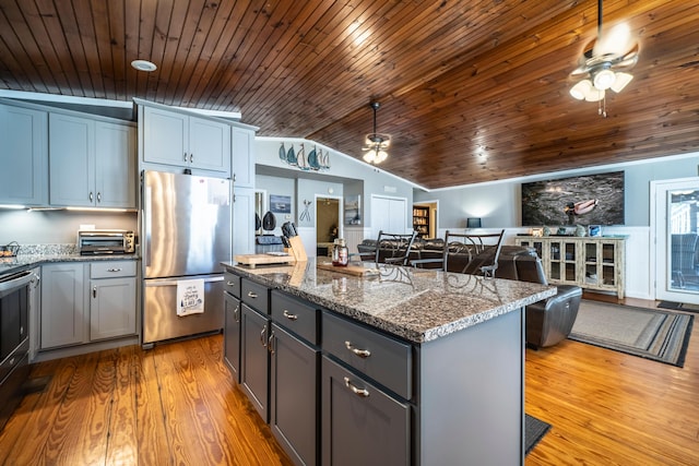 kitchen featuring a center island, vaulted ceiling, stainless steel fridge, dark stone countertops, and light wood-type flooring