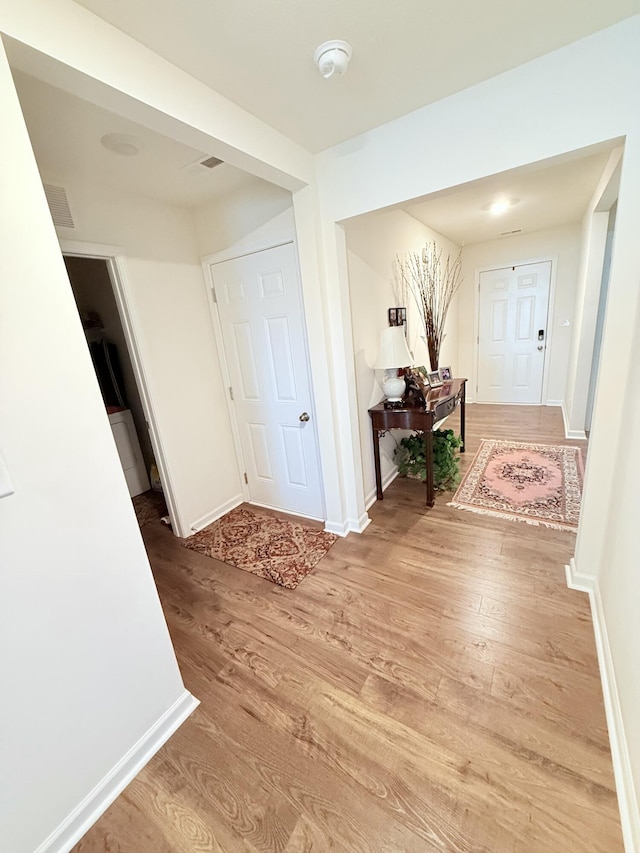 hall featuring visible vents, baseboards, and light wood-style floors