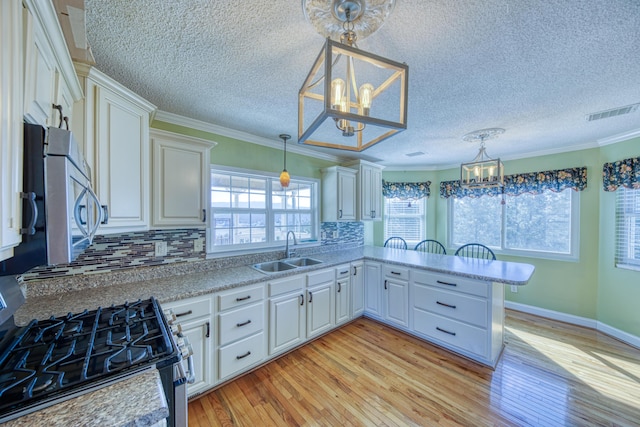 kitchen with light wood-type flooring, a notable chandelier, a sink, appliances with stainless steel finishes, and white cabinets