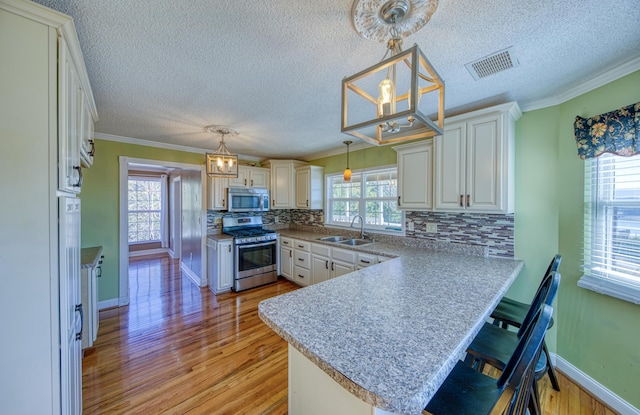 kitchen featuring visible vents, a sink, appliances with stainless steel finishes, a peninsula, and light wood finished floors