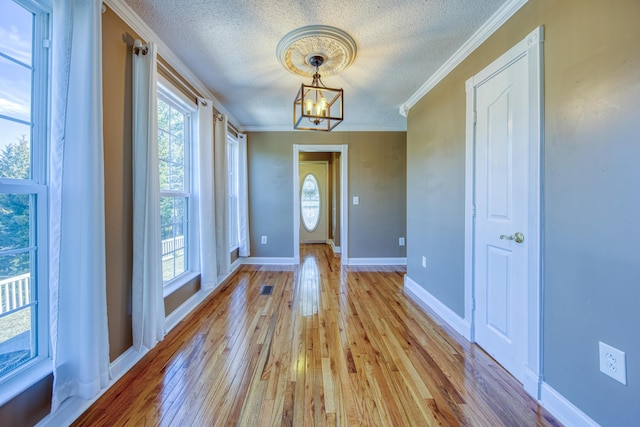 entryway featuring a textured ceiling, an inviting chandelier, light wood-type flooring, and ornamental molding