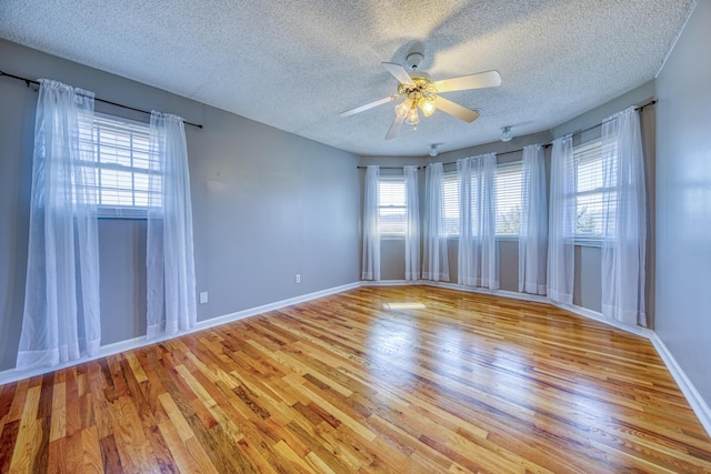 spare room featuring a ceiling fan, light wood-style floors, baseboards, and a textured ceiling