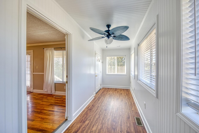 interior space with visible vents, ornamental molding, ceiling fan, and wood finished floors