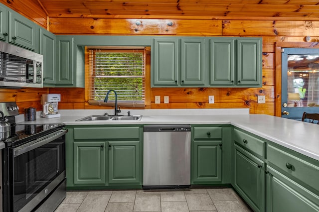 kitchen featuring green cabinetry, stainless steel appliances, wooden walls, and sink