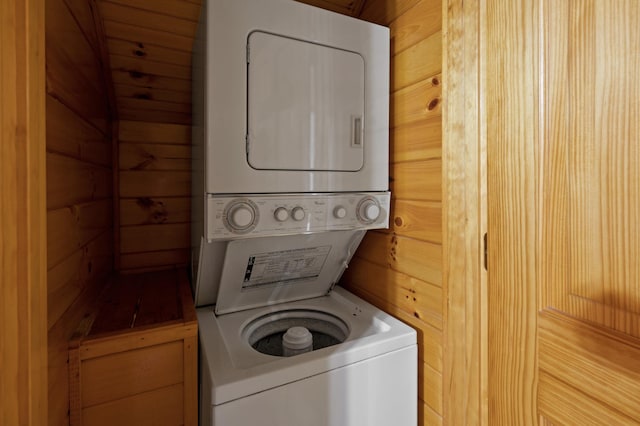 washroom with stacked washer / drying machine and wood walls