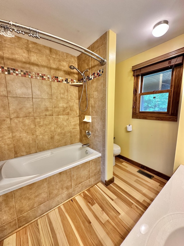 bathroom featuring tiled shower / bath combo, toilet, and wood-type flooring