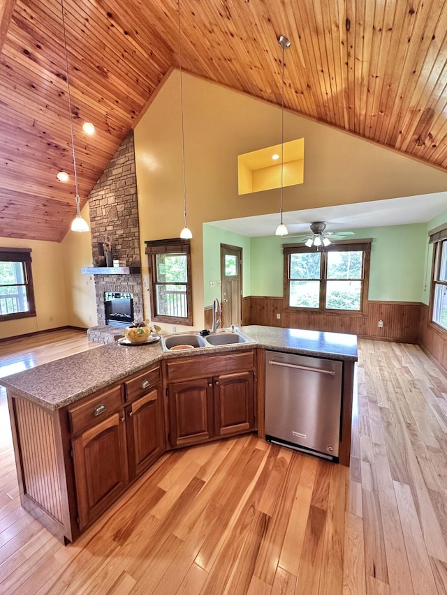 kitchen with dishwasher, a center island with sink, sink, wooden walls, and decorative light fixtures