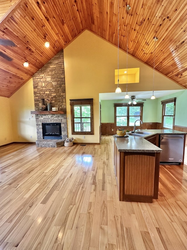 kitchen with sink, hanging light fixtures, stainless steel dishwasher, a fireplace, and light wood-type flooring