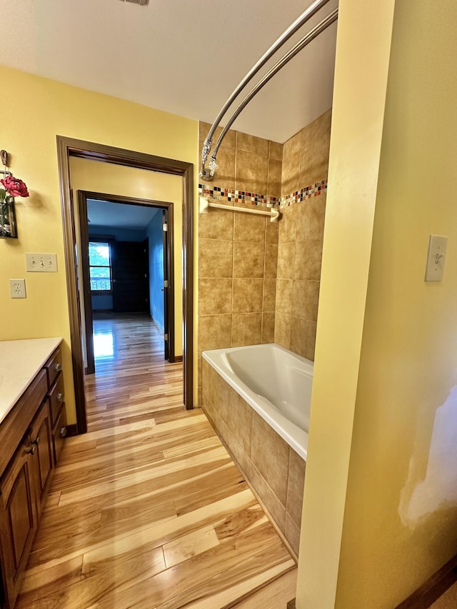 bathroom with hardwood / wood-style flooring, vanity, and tiled shower / bath combo