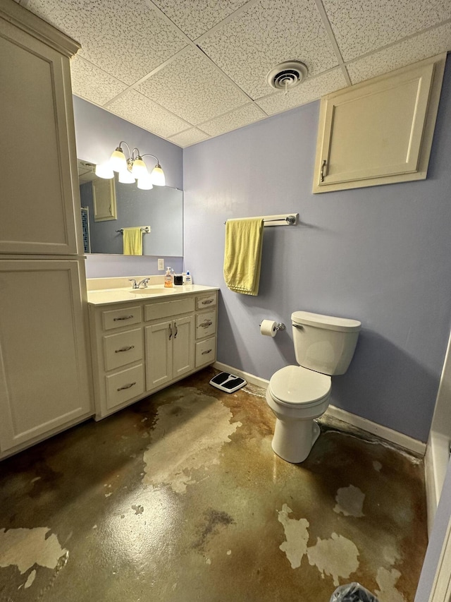 bathroom with a drop ceiling, vanity, concrete flooring, and toilet