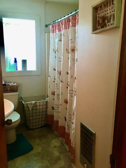 bathroom with curtained shower, toilet, and heating unit