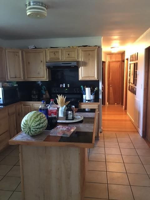 kitchen with ventilation hood, light brown cabinets, light tile patterned floors, and black / electric stove