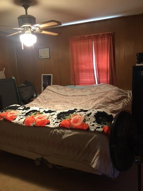 bedroom featuring carpet, ceiling fan, and wooden walls