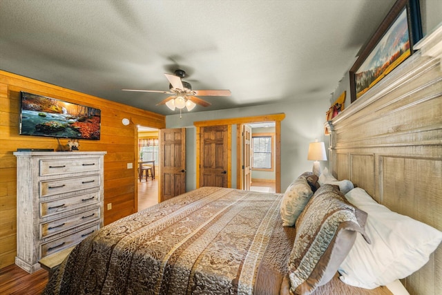 bedroom with a textured ceiling, wood-type flooring, ceiling fan, and wood walls