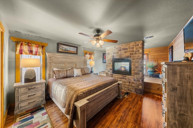 bedroom with ceiling fan, a multi sided fireplace, dark hardwood / wood-style flooring, and a textured ceiling