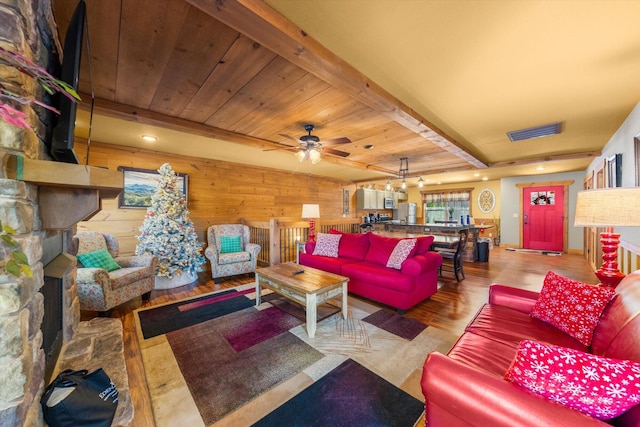 living room with beamed ceiling, wood walls, a fireplace, and light hardwood / wood-style flooring