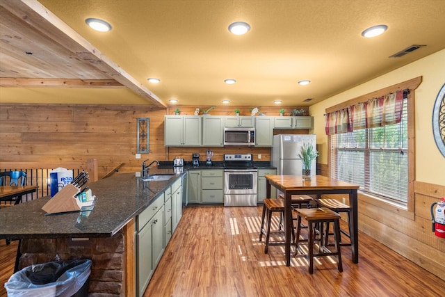 kitchen with sink, wood walls, light hardwood / wood-style flooring, appliances with stainless steel finishes, and dark stone counters