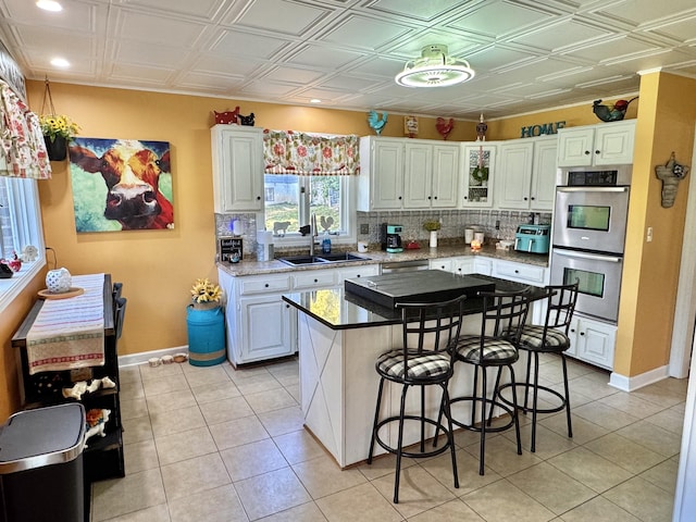 kitchen with double oven, white cabinets, sink, and a kitchen island