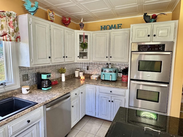 kitchen featuring sink, light tile patterned floors, dark stone countertops, white cabinets, and appliances with stainless steel finishes