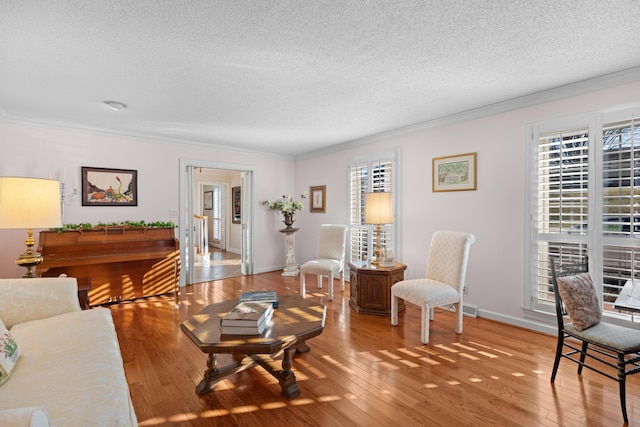 living room featuring crown molding, a textured ceiling, baseboards, and hardwood / wood-style floors