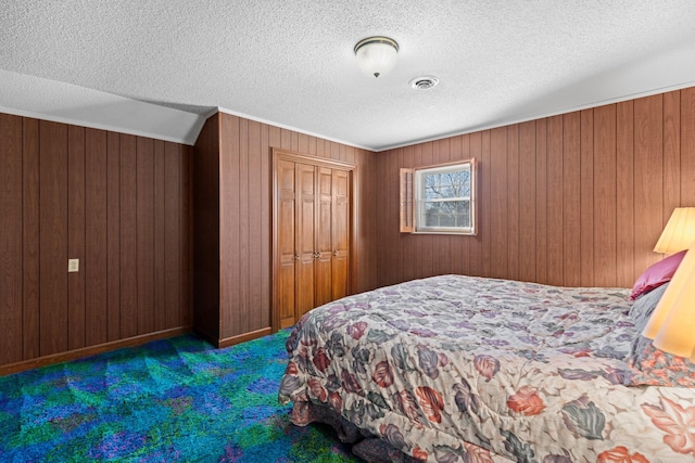 bedroom with visible vents, a textured ceiling, carpet flooring, wood walls, and a closet