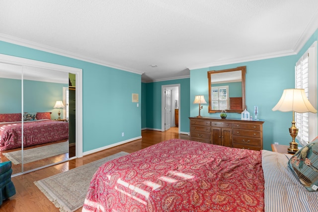 bedroom with a textured ceiling, wood finished floors, baseboards, ornamental molding, and a closet