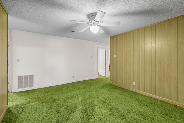 carpeted spare room featuring a textured ceiling, wooden walls, visible vents, baseboards, and a ceiling fan