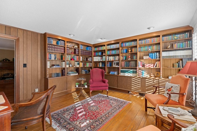 sitting room with a textured ceiling, wood walls, wall of books, and hardwood / wood-style flooring