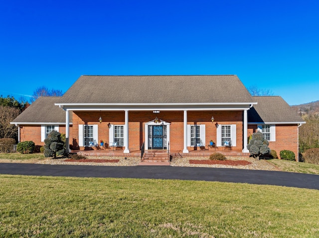 view of front facade featuring covered porch, roof with shingles, a front lawn, and brick siding