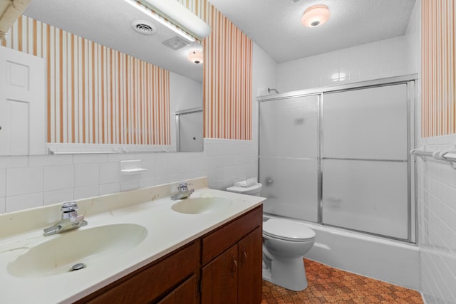 full bath with a textured ceiling, tile walls, bath / shower combo with glass door, and a sink