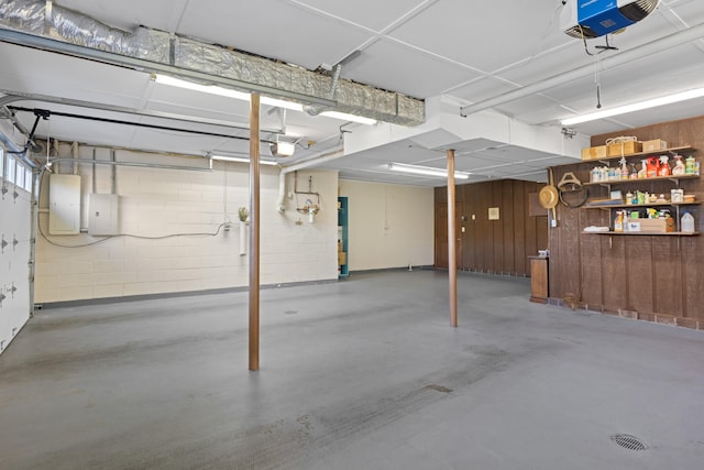 garage with concrete block wall, electric panel, and a garage door opener