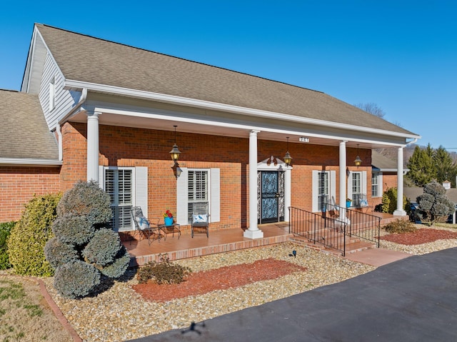 view of front of house with roof with shingles, a porch, and brick siding