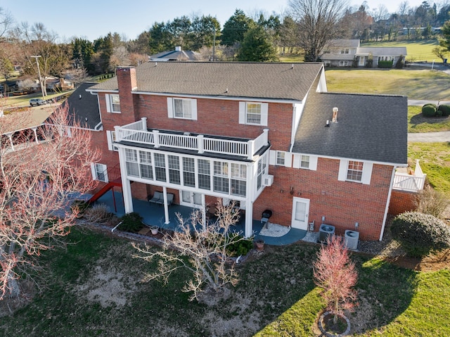 rear view of property with cooling unit, a patio area, brick siding, and a chimney