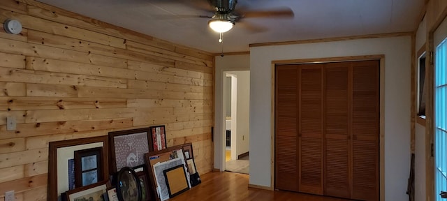 bedroom featuring ornamental molding, ceiling fan, hardwood / wood-style floors, a closet, and wood walls