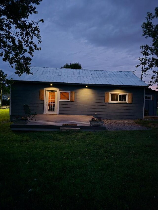 back house at dusk featuring a lawn and a wooden deck