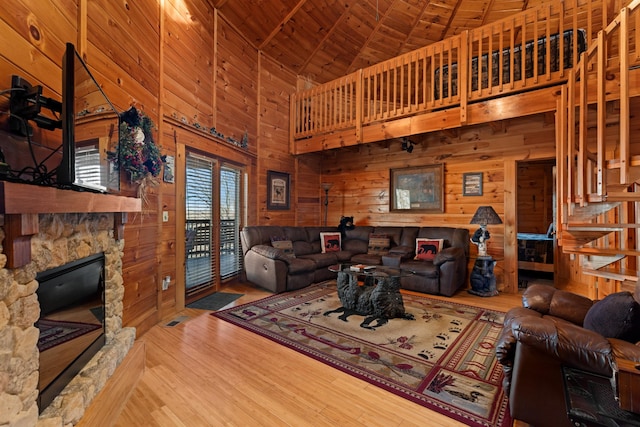 living area featuring lofted ceiling, a stone fireplace, wooden walls, wood finished floors, and wood ceiling