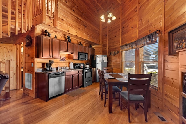 kitchen with wooden walls, visible vents, light wood-style flooring, appliances with stainless steel finishes, and high vaulted ceiling