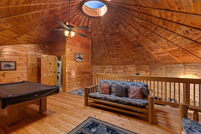 game room with wooden walls, stacked washer and clothes dryer, wooden ceiling, hardwood / wood-style floors, and vaulted ceiling