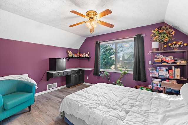bedroom featuring lofted ceiling, wood finished floors, visible vents, baseboards, and a textured ceiling