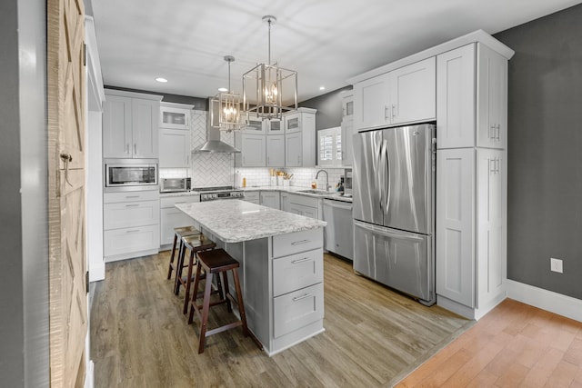 kitchen featuring appliances with stainless steel finishes, wall chimney range hood, a sink, a chandelier, and a breakfast bar area